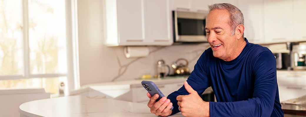 Image of male hearing aid wearer giving a thumbs up to his mobile phone screen